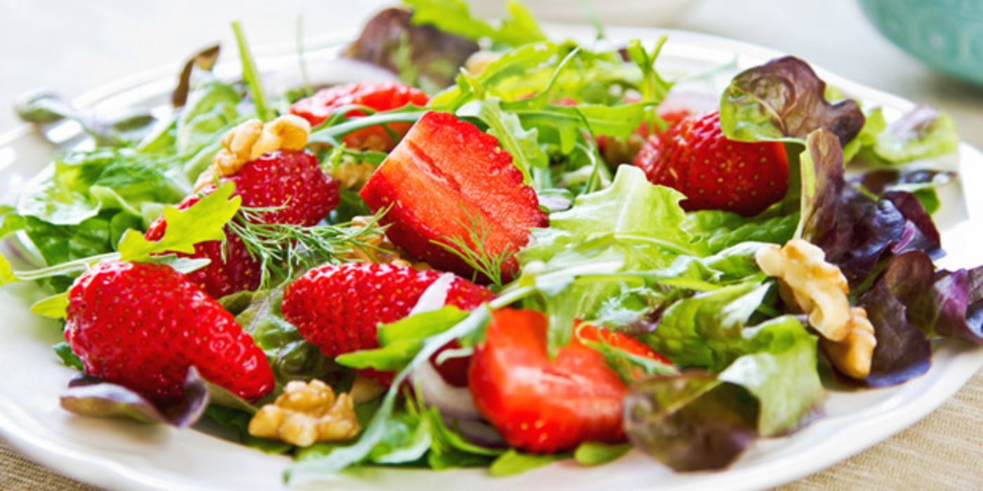 Bunte Blattsalate mit Erdbeeren und Walnüssen auf weißem Teller