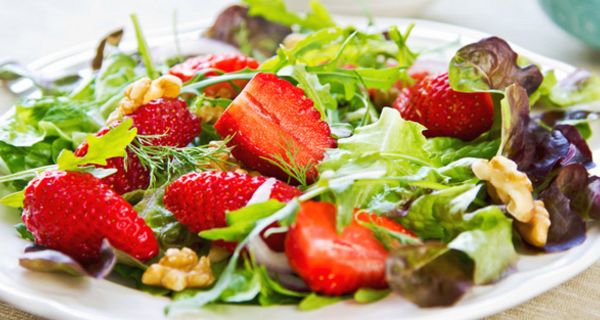 Bunte Blattsalate mit Erdbeeren und Walnüssen auf weißem Teller