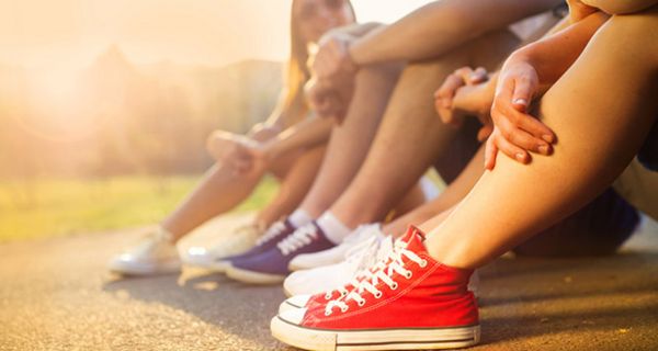 Nackte Beine von jungen Frauen die am Boden sitzen in Abendlicht, alle mit Sneakers (Chucks?), im Vordergrund rote mit weißen Sohlen