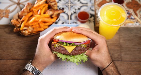 Mann, hält einen Cheeseburger in der Hand.