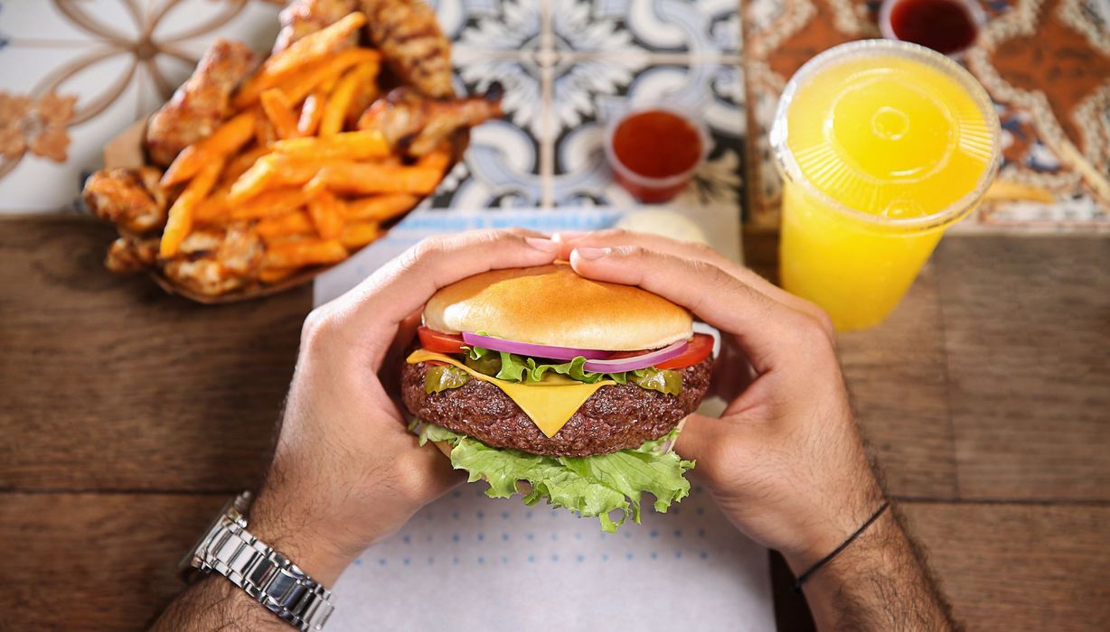 Mann, hält einen Cheeseburger in der Hand.