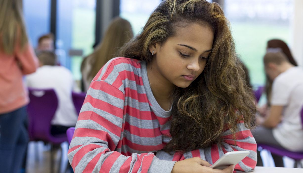 Jugendliche, sitzt in der Schule mit ihrem Smartphone.