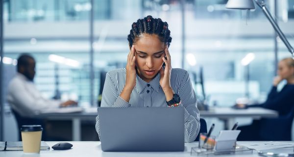 Frau, sitzt mit Migräne am Arbeitsplatz.