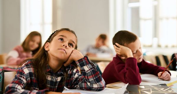 Ein Mädchen und ein junge sitzen nebeneinander im Klassenzimmer und das Mädchen schaut an die Decke.