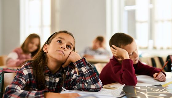 Ein Mädchen und ein junge sitzen nebeneinander im Klassenzimmer und das Mädchen schaut an die Decke.