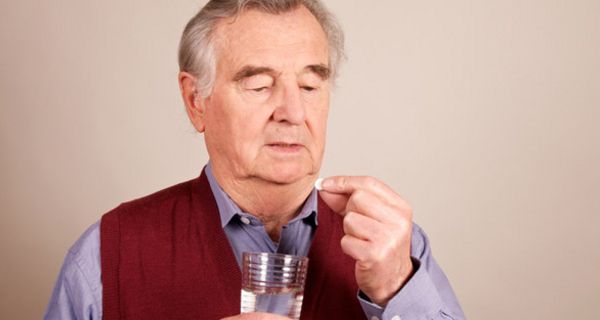 Senior nimmt eine Tablette mit einem Glas Wasser ein