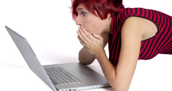Junge Frau blickt erstaunt auf Computerbildschirm.
