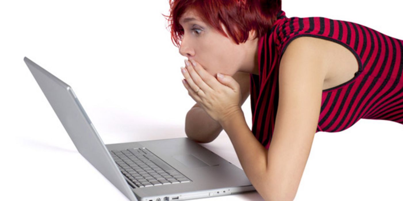Junge Frau blickt erstaunt auf Computerbildschirm.