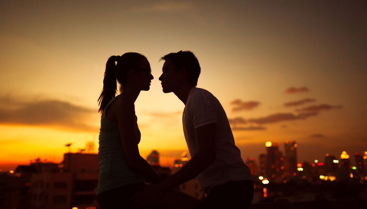 Zwei Jugendliche sitzen sich gegenüber, Sonnenuntergang im Hintergrund.
