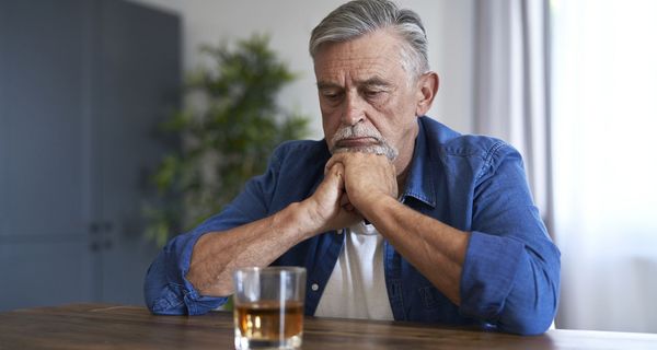 Mann, sitzt vor einem Glas Alkohol.