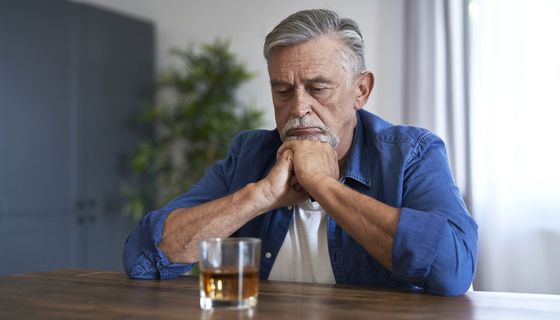 Mann, sitzt vor einem Glas Alkohol.