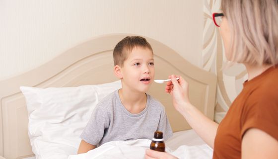 Mutter gibt Sohn Arzneimittel-Saft auf einem Löffel.