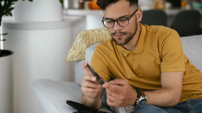 Junger Mann sitzt auf dem Sofa und misst seinen Blutzucker.