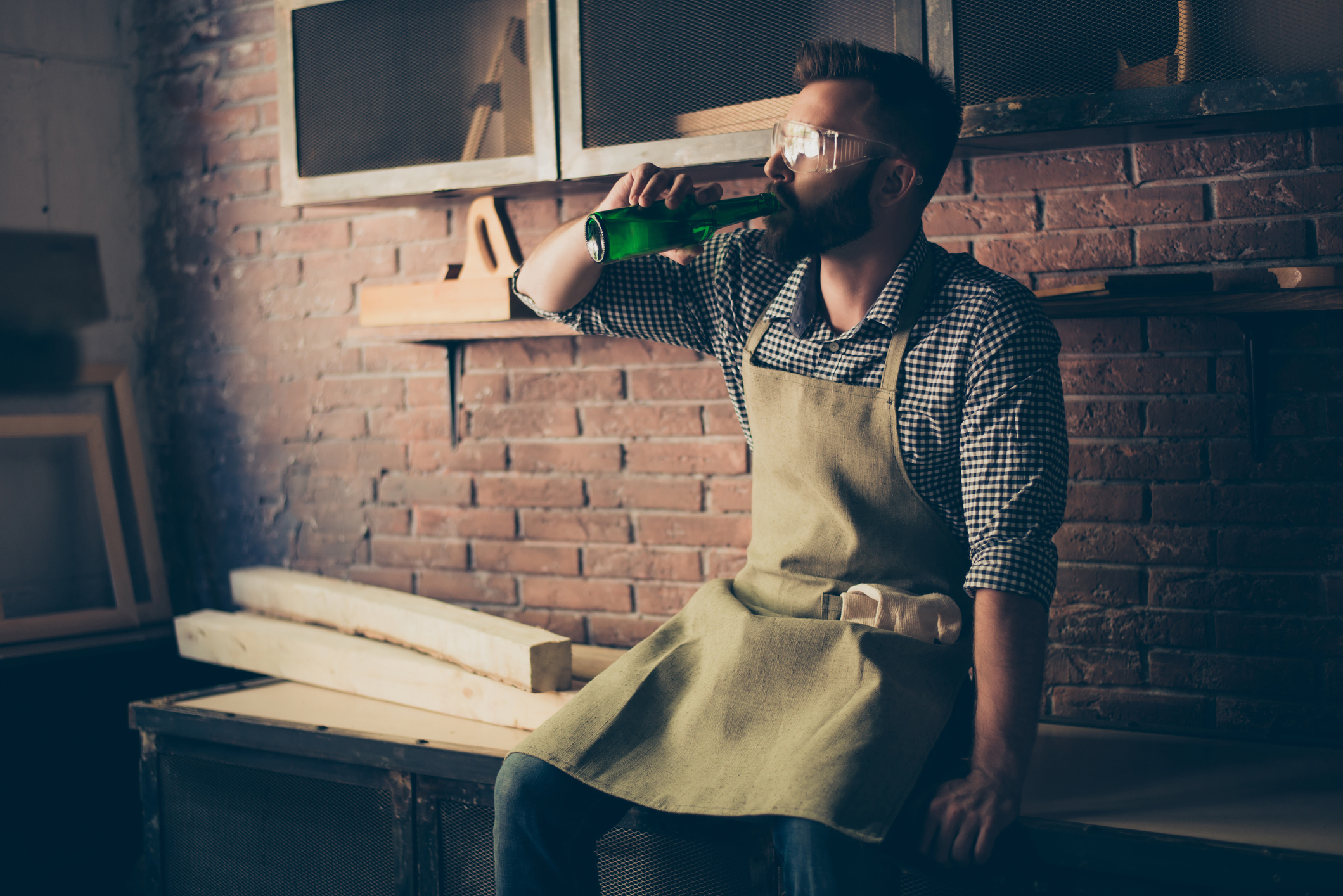 Handwerker, sitzt auf Arbeitsbank und trinkt ein Bier.