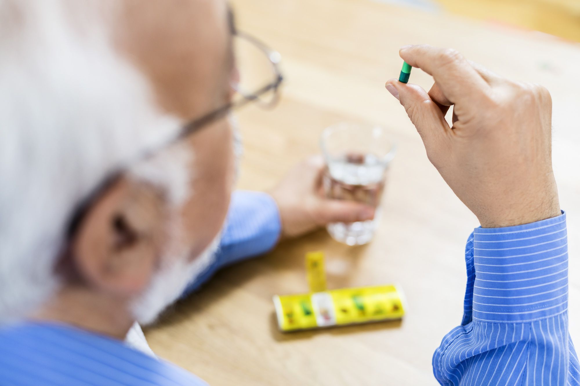 Älterer Mann mit Pillendose und einer Tablette in der Hand.