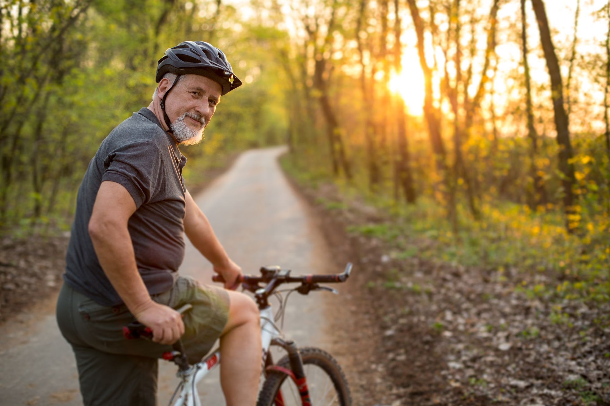 Älterer Herr mit leichtem Bauchansatz, Fahrrad und Helm auf einem Waldweg.