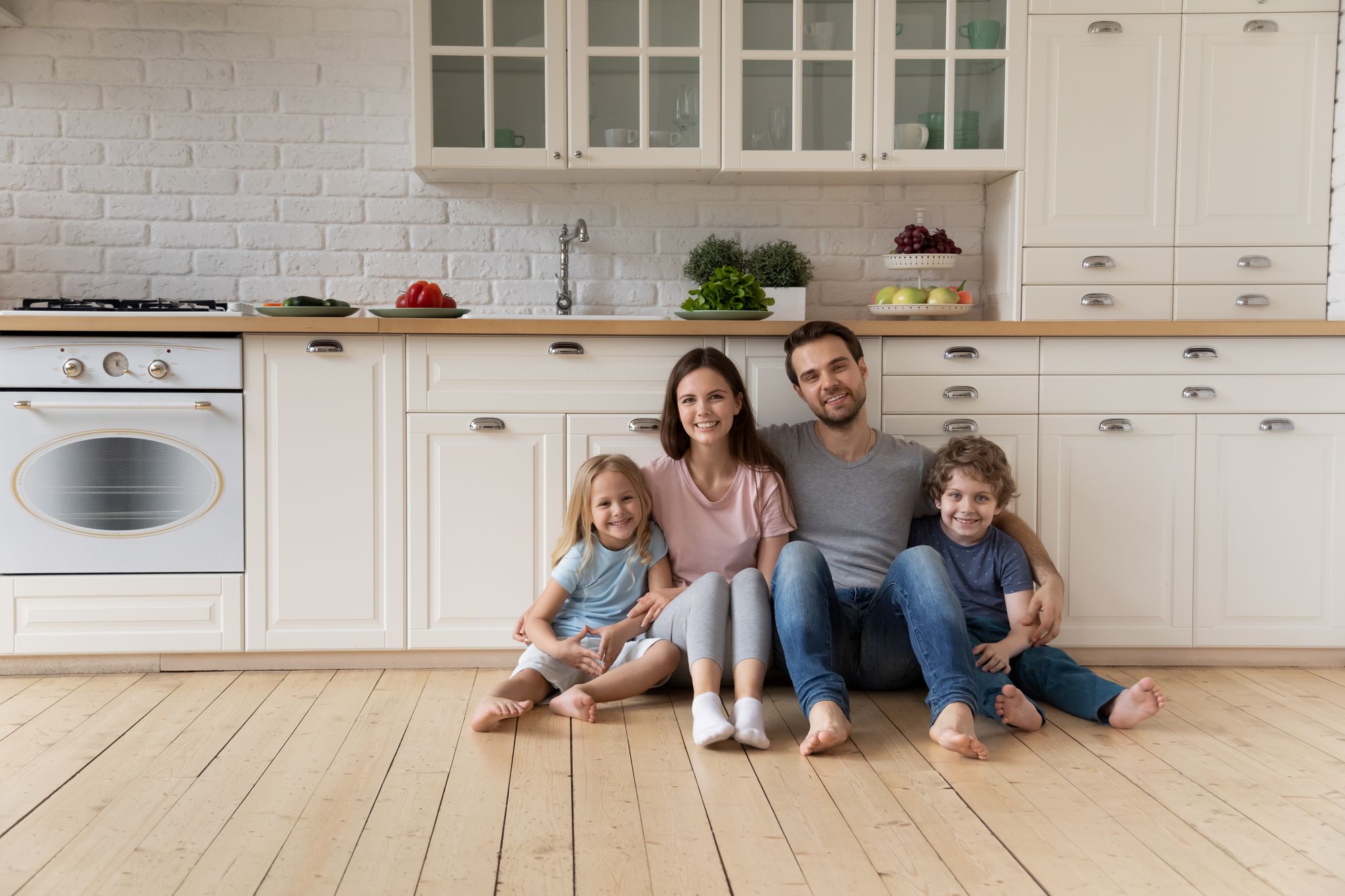 Gutgelaunte Familie mit zwei kleinen Kindern sitzt zusammen auf dem Küchenfußboden.